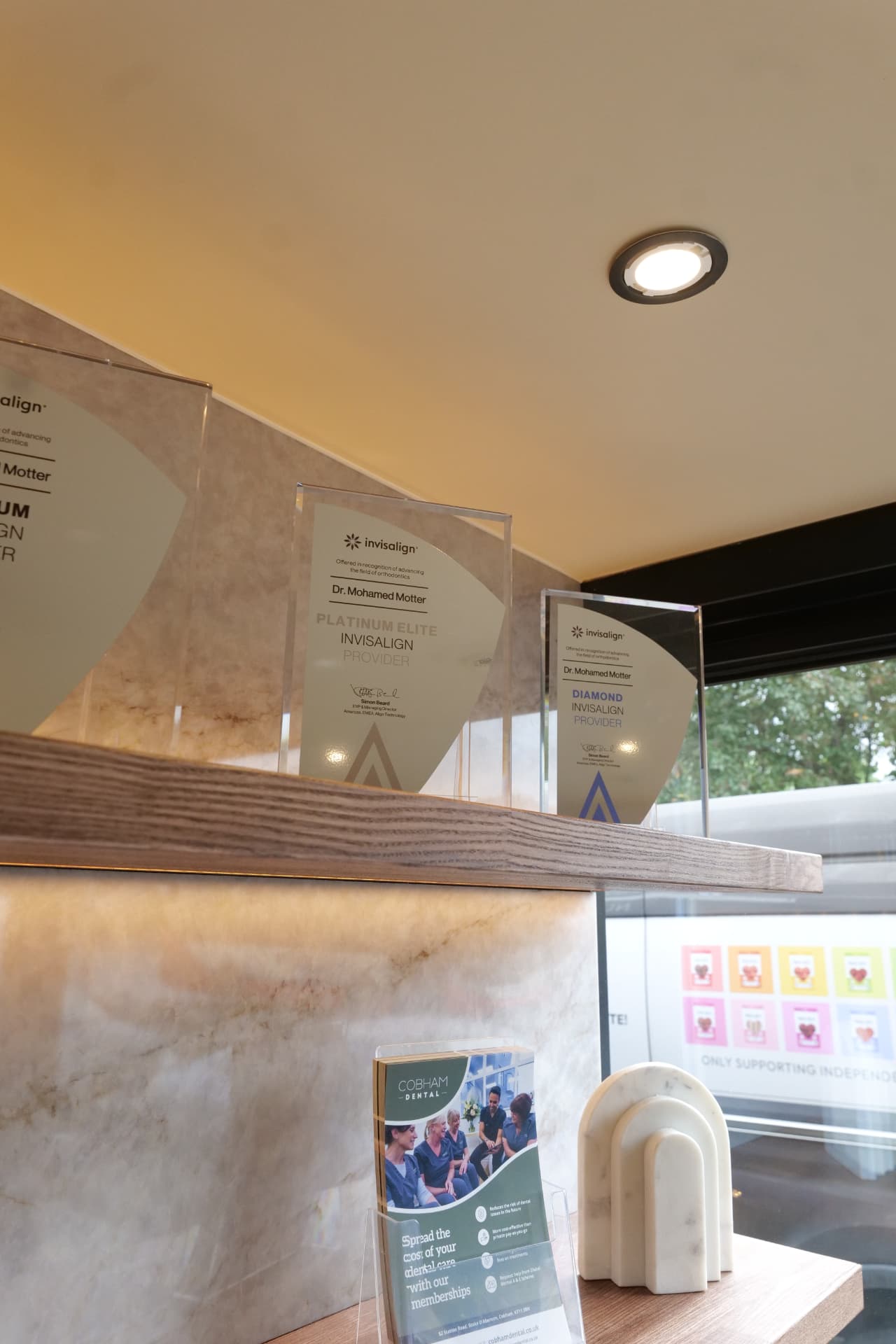 Invisalign provider award plaques on the windowsill by the entrance at Cobham Dental, looking out to Station Road