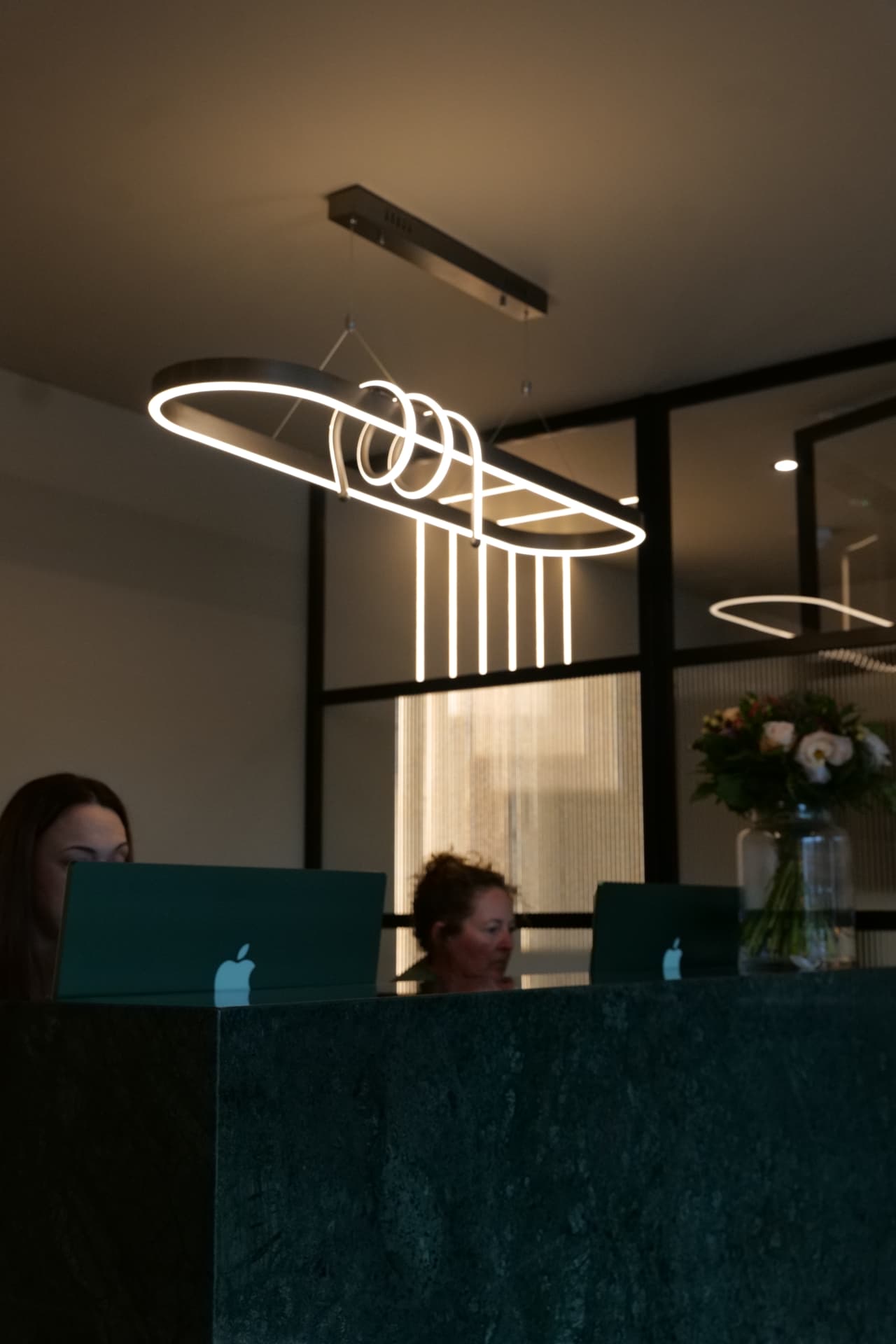 Two members of the Cobham Dental reception team working at the reception desk under a sculptural ring light